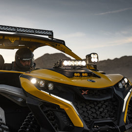 Baja Designs Can-Am Maverick R Clear 10in OnX6+ Shock Tower Kit installed on a yellow UTV, showcasing powerful off-road lighting.